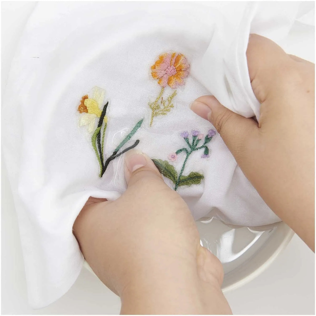 Hands rinsing water-soluble adhesive backing from embroidered spring flowers in water