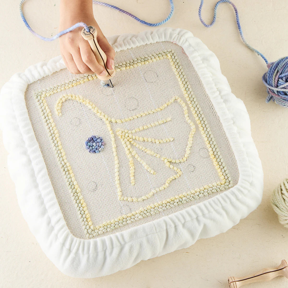 Hand using punch needle tool on white fleece covered frame for bird tufting pattern