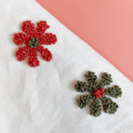 Close-up of textured loop stitches on tufted red and olive green yarn flowers