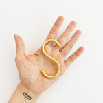 Matt gold S-hook detail on plain background